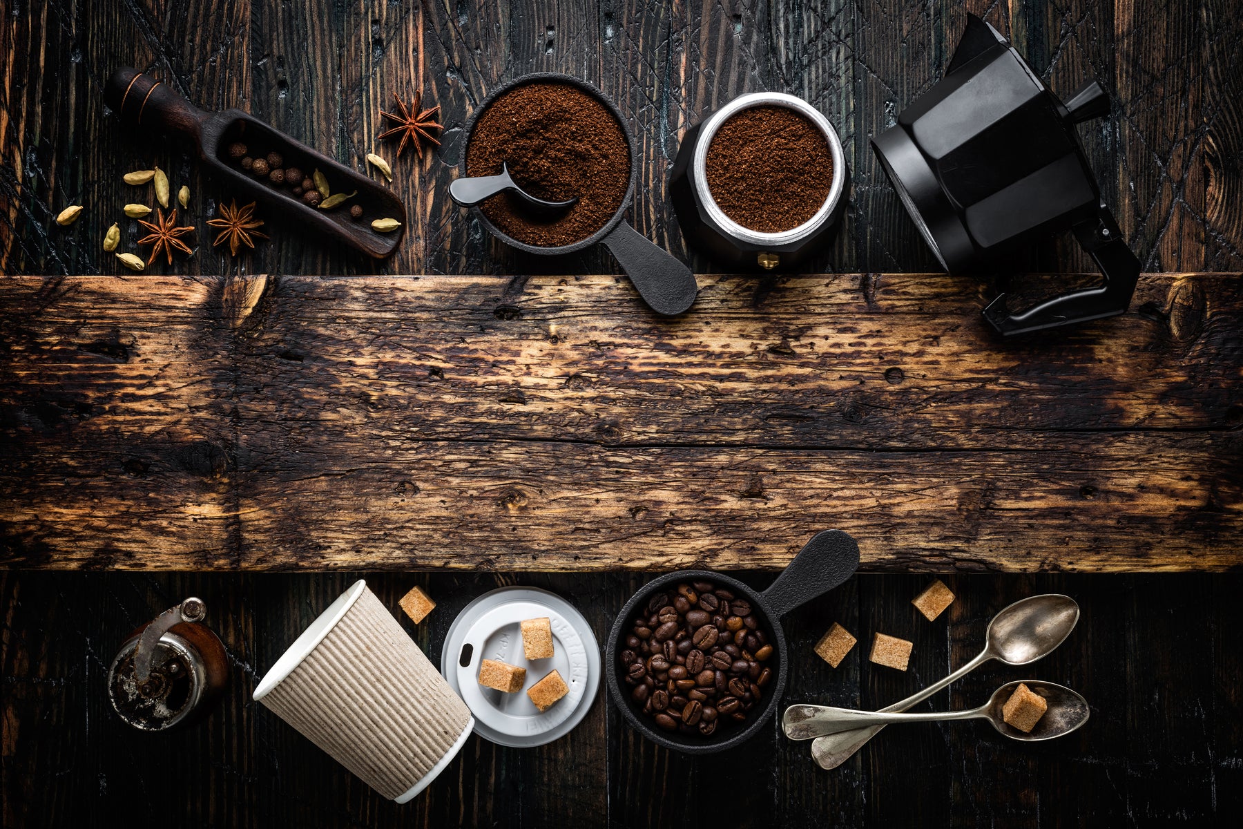 Overhead photo of coffee beans, grounds, spices, sugar, cups, grinders on wood